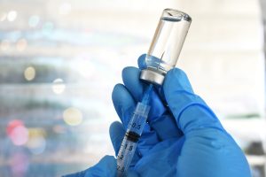 Hand holding syringe inserted in vaccine vial