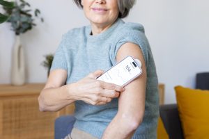 Mature adult woman checking glucose monitor with smartphone